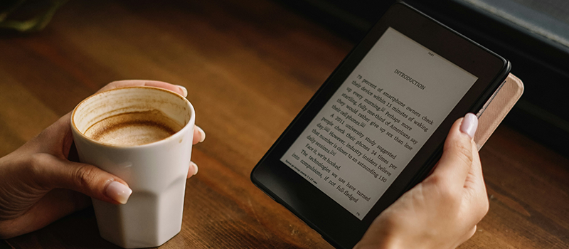 Person with coffee in one hand and eReader in the other