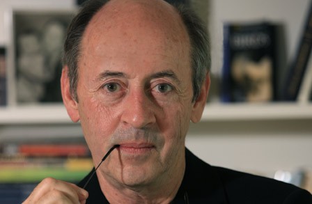 A balding man is holding a pipe in his mouth.