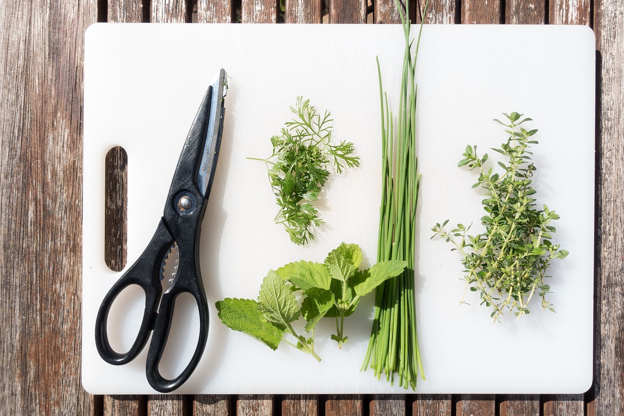 A cutting board with a pair of scissors and an assortment of fresh herbs.