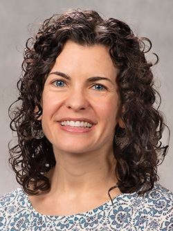 A smiling woman with dark, curly, shoulder-length hair