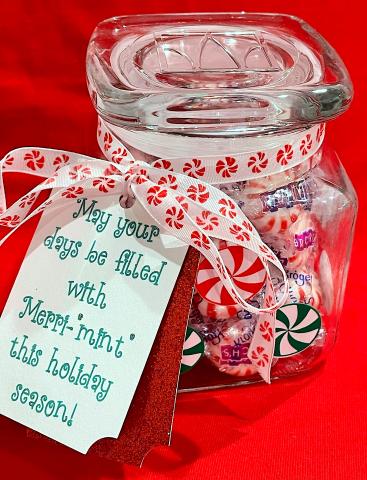 A glass jar with a gift tag; jar is filled with holiday peppermint candies.