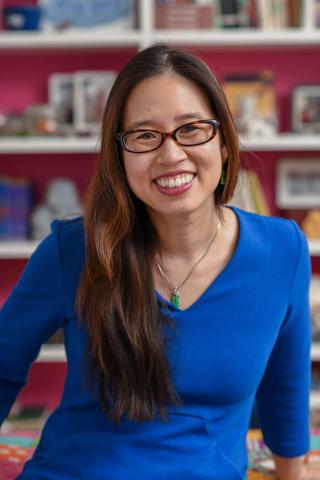 An Asian woman with long hair and glasses is wearing a blue shirt.