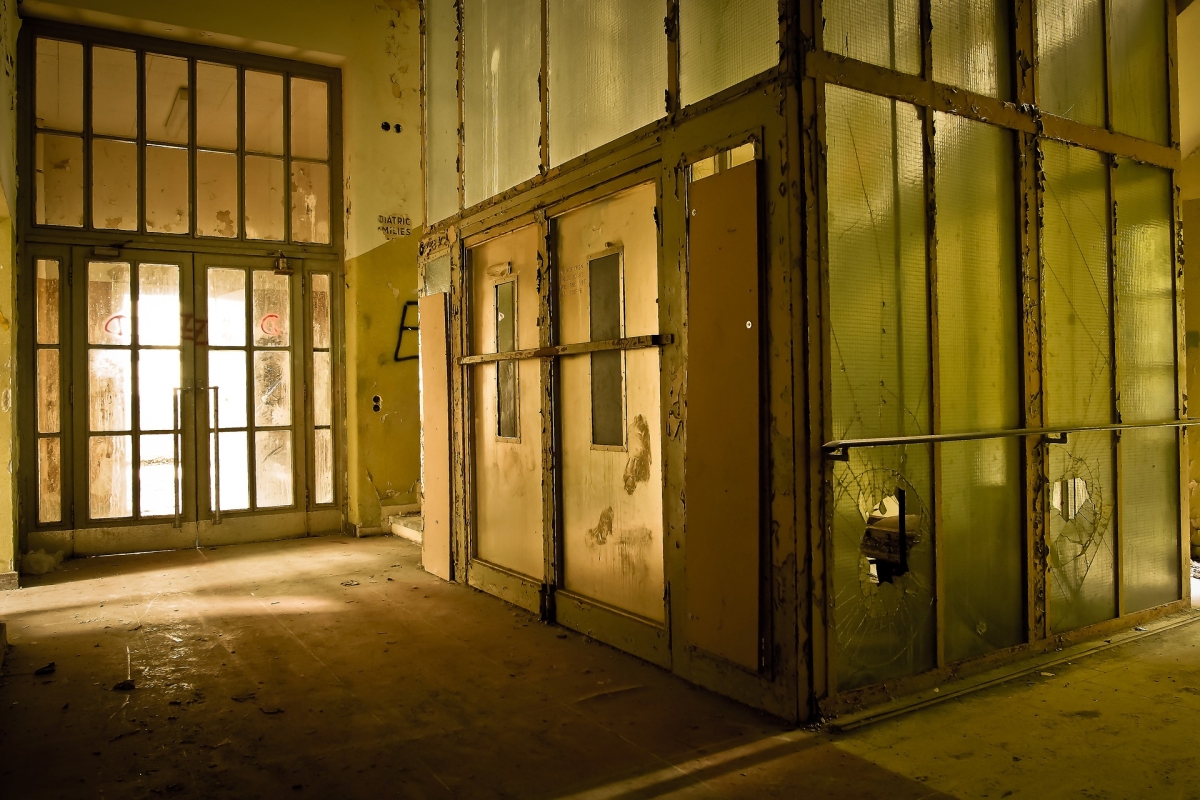 Double doors inside an abandoned building leading to a room with broken glass walls.