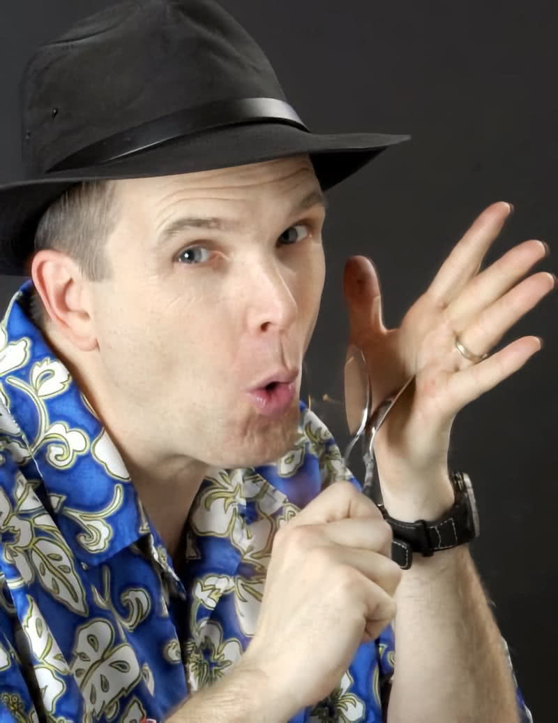 A man in a black hat holding two spoons next to his face.