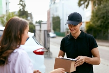 Man holding woman a package by the tail end of vehicle