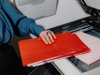 Hand holding red folders and placing white paper down on top of printer scanner