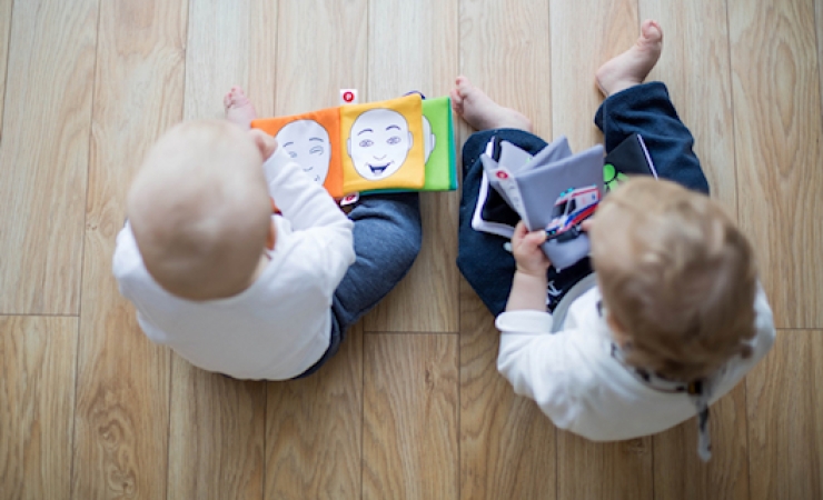 Two babies sitting on the floor and looking through picture books