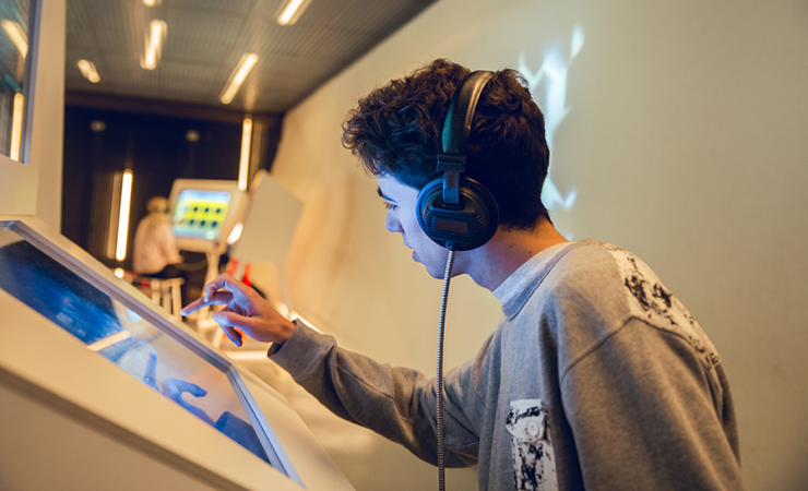 Teen boy using an interactive touch screen in a museum with headphones on his head